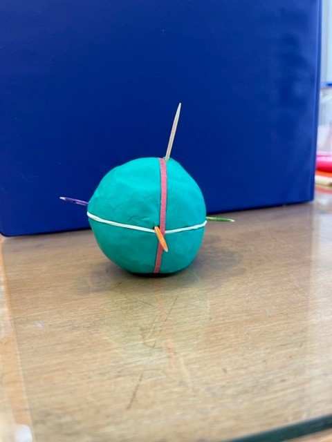 A blue clay ball with two rubber bands around its axis and through it.